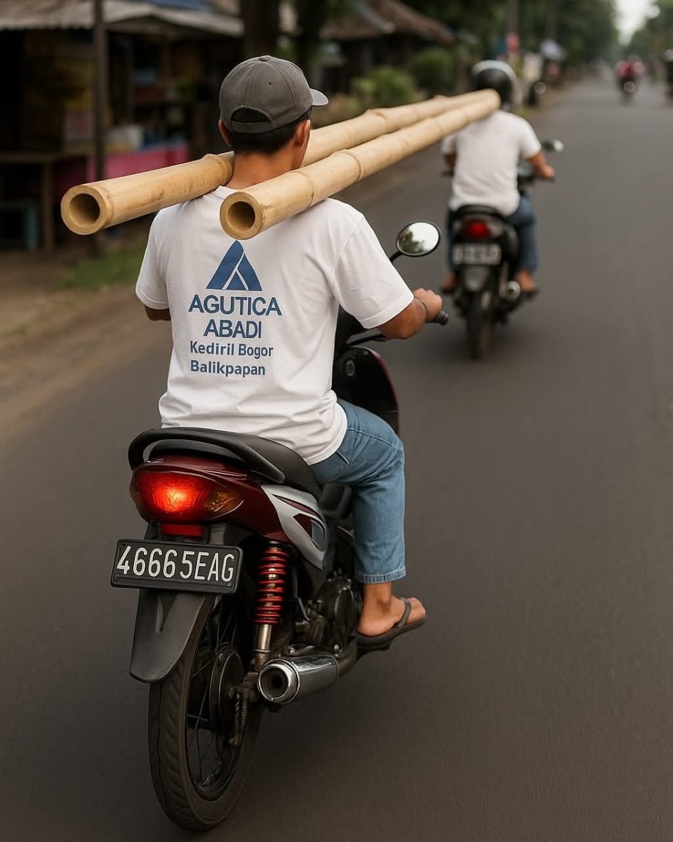 Motorkár prepravuje bambusové tyče na vidieckej ceste, oblečený v tričku s nápisom.
