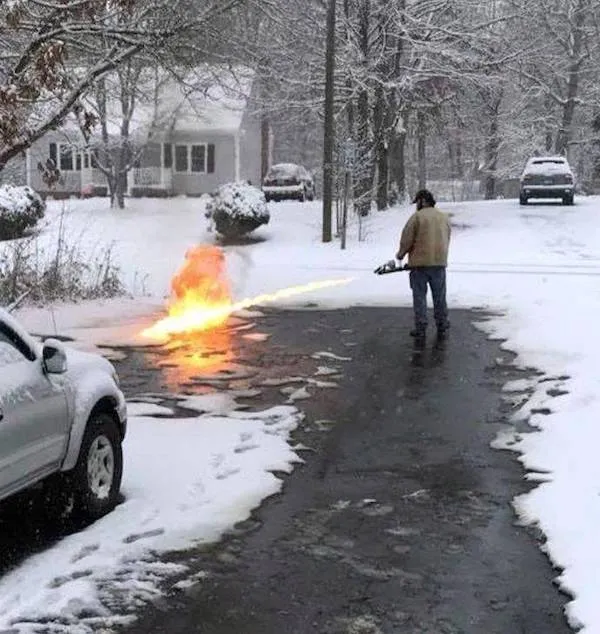 Muž pomocou plameňometu odstraňuje sneh na príjazdovej ceste počas zasneženého zimného dňa.