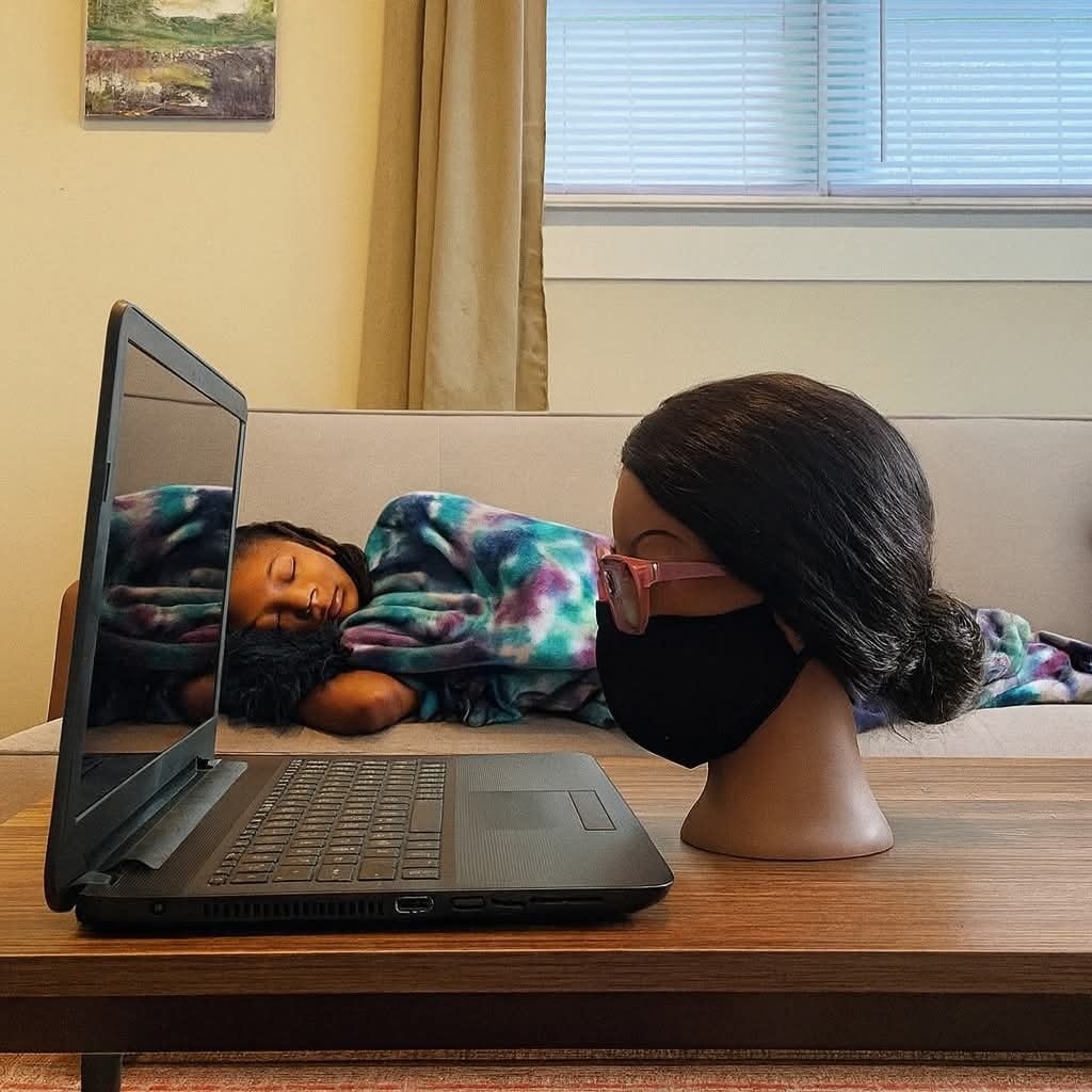 Dievčatko spí na gauči vedľa notebooku a figuríny s okuliarmi, ktorá vyzerá, akoby sedela pri počítači.