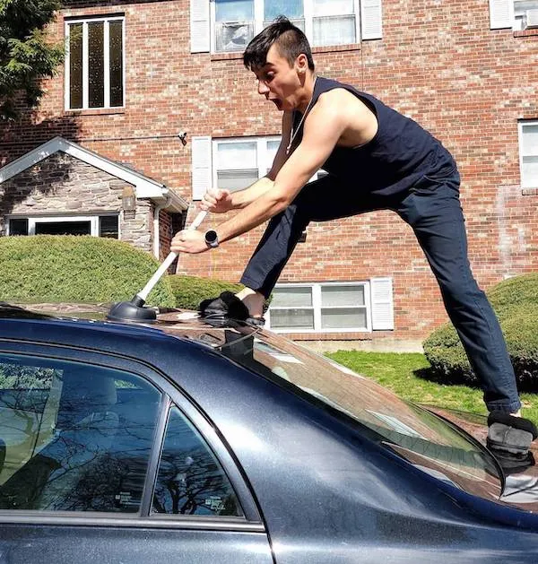 Osoba naťahujúca sa na streche auta, používajúc pritom záchodový zvon v komickej situácii.