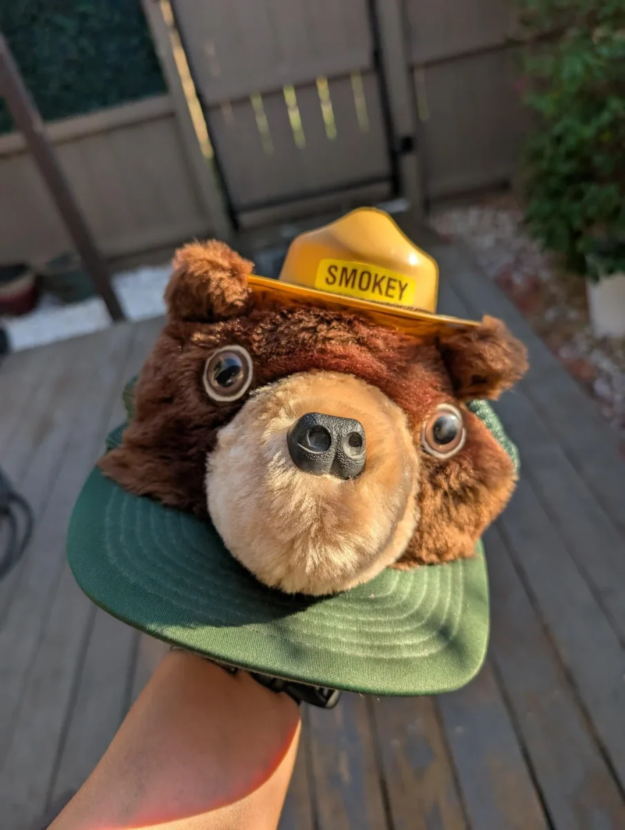 Čiapka s plyšovou tvárou medveďa a textom Smokey na vonkajšej terase za slnečného dňa.