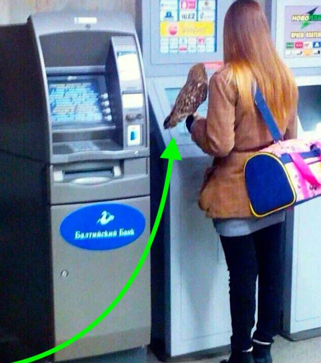 Žena s taškou a sokolom na ruke používa bankomat vedľa automatu na lístky.