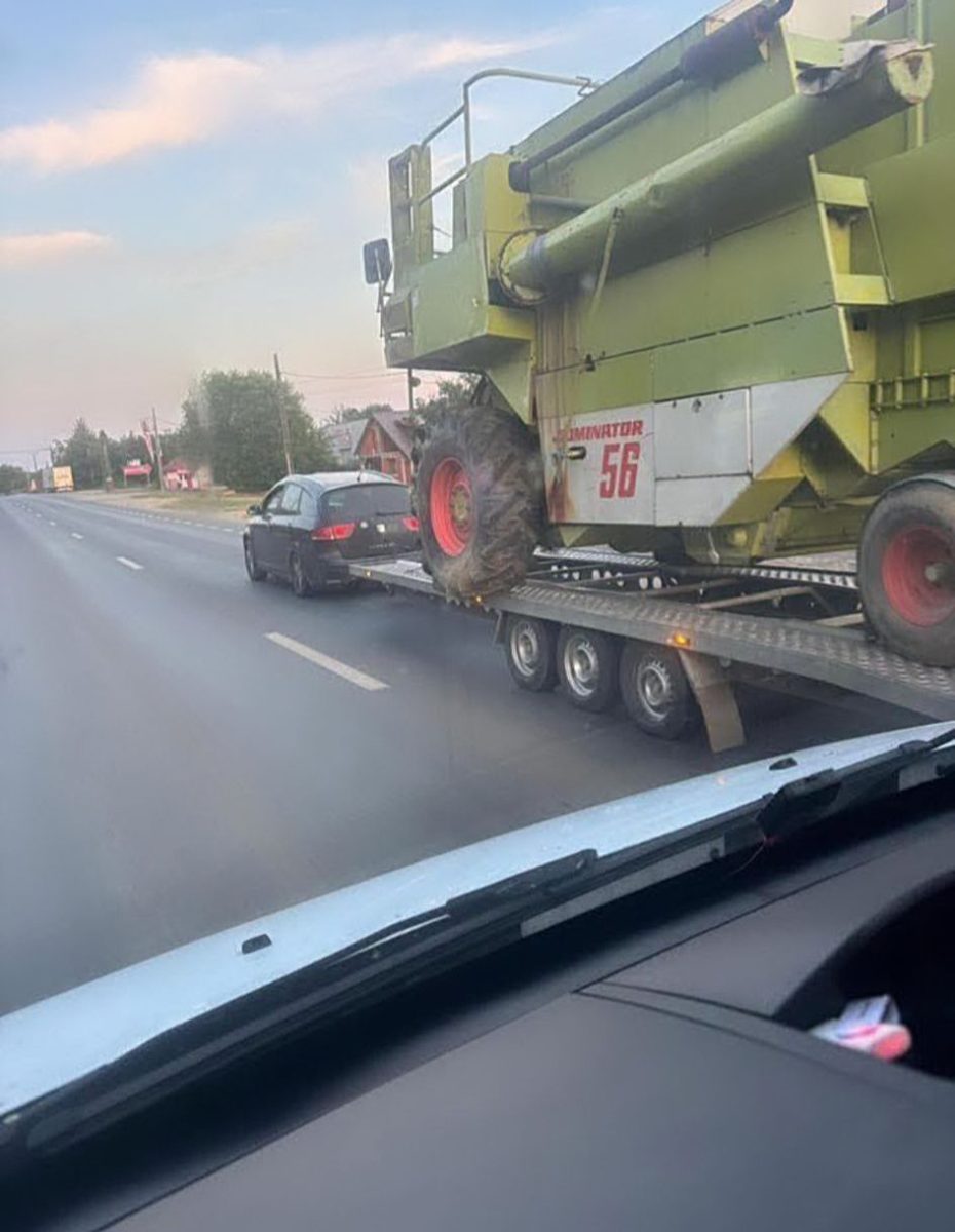Osobné auto ťahá veľký kombajn na prívesnom vozíku po ceste, nezvyčajná situácia na doprave.