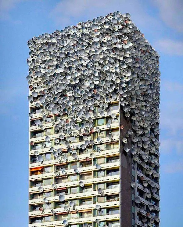 Vysoká budova pokrytá stovkami satelitných antén na modrom pozadí oblohy.