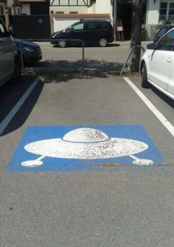 Parkovacie miesto s piktogramom UFO pre fanúšikov sci-fi na mestskom parkovisku.