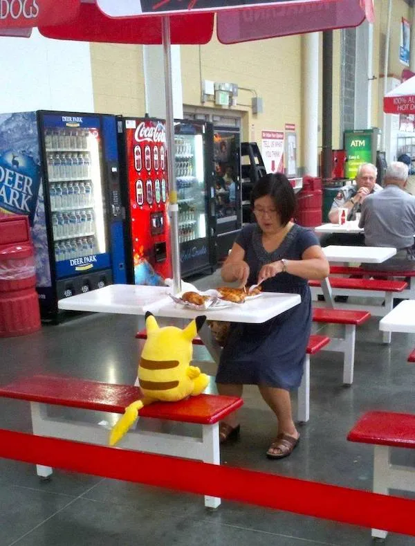 Žena obeduje s plyšovým Pikachu pri stole vo vnútri reštaurácie s automatmi na nápoje v pozadí.