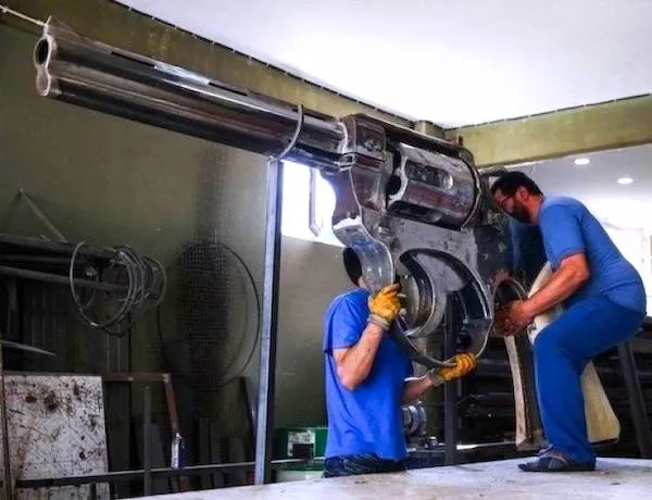 Dvaja muži pracujú na veľkej kovovej soške revolvera v dielni.