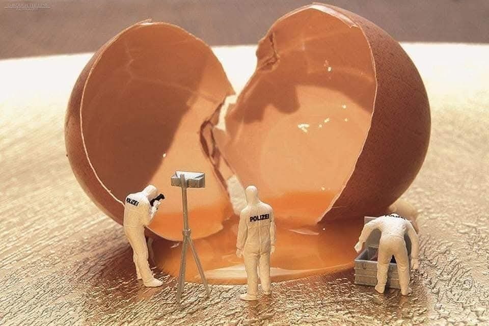 Miniatúrni vyšetrovatelia skúmajú miesto zločinu s puknutým vajíčkom na zlatom povrchu.