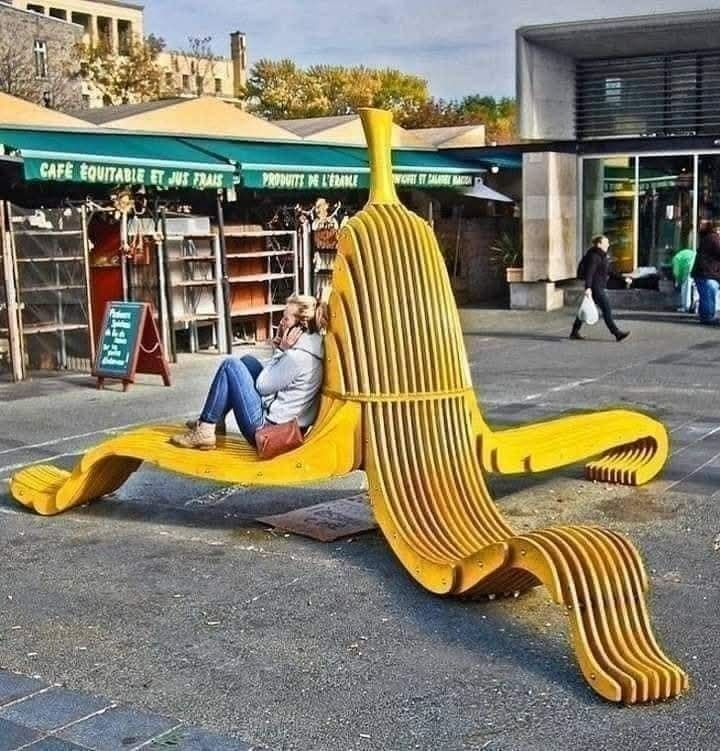 Osoba sedí na lavičke v tvare banánovej šupky v mestskom prostredí.