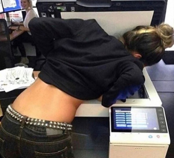 Osoba skúma fotokopírku zblízka, pričom v kancelárii je pozadie s variabilnou aktivitou.