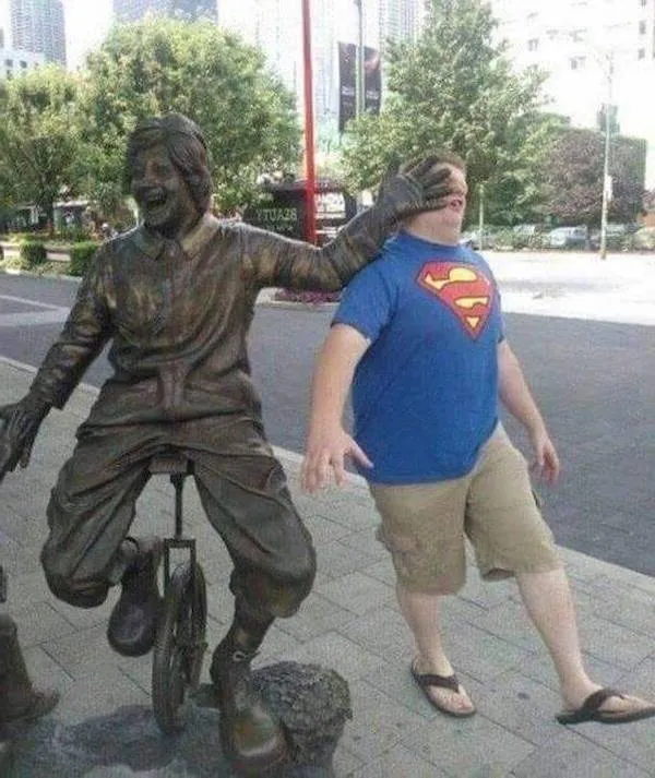 Socha na jednokolke zdanlivo zakrýva oči mužovi v tričku Supermana na ulici.