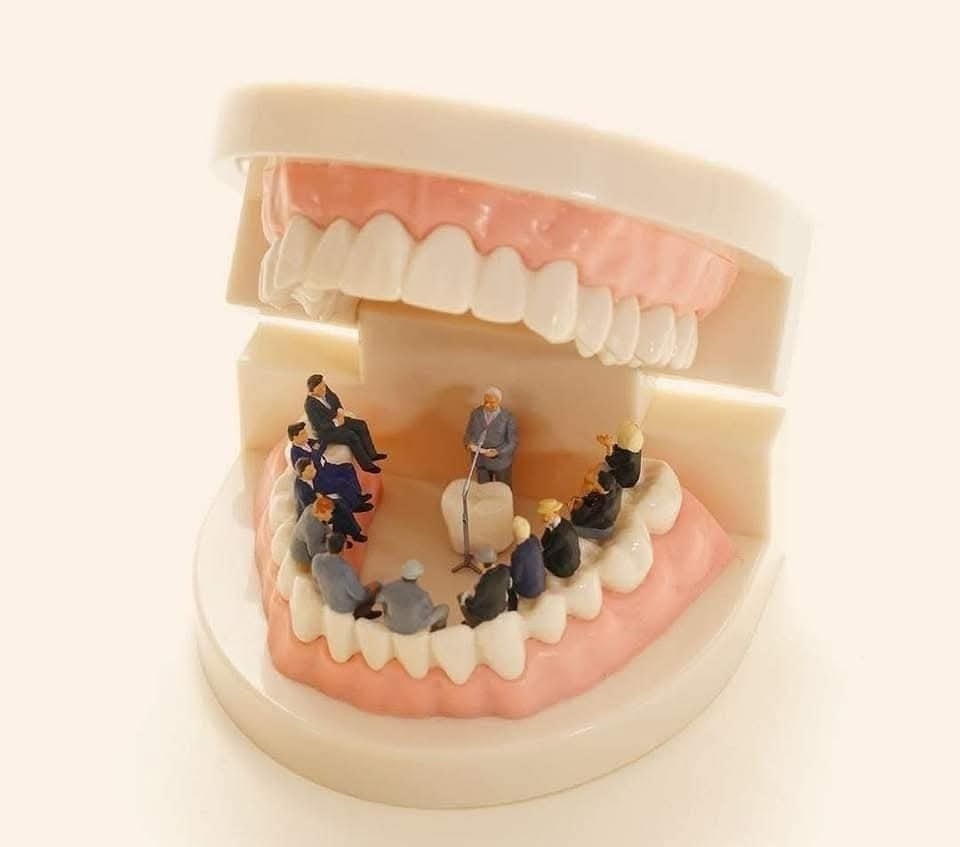 Miniatúrne konferenčné stretnutie vo vnútri modelu zubov, prezentujúci v strede s publikom okolo.