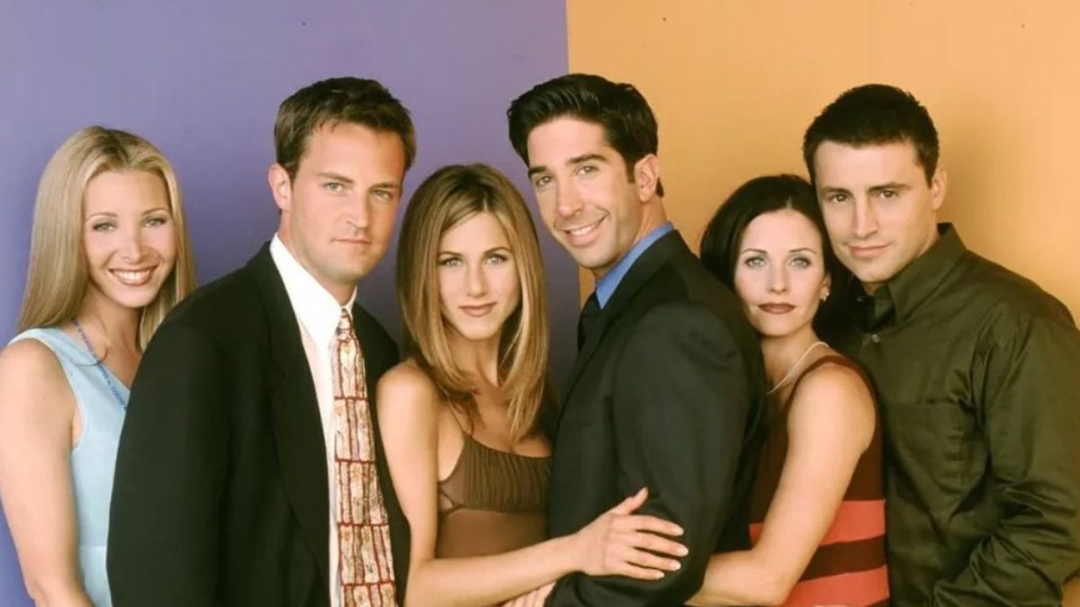 Skupina šiestich priateľov stojí vedľa seba pred dvojfarebným pozadím.