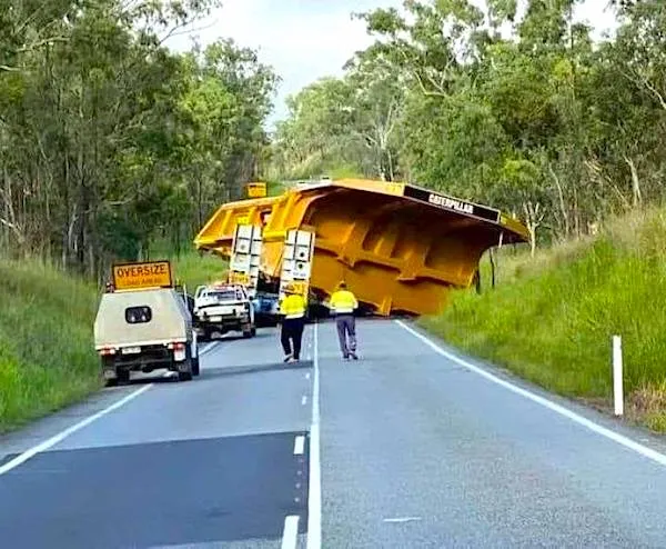 Obrovský náklad blokuje cestu v lese, doprovodné vozidlo upozorňuje bezpečnostným nápisom Oversize.