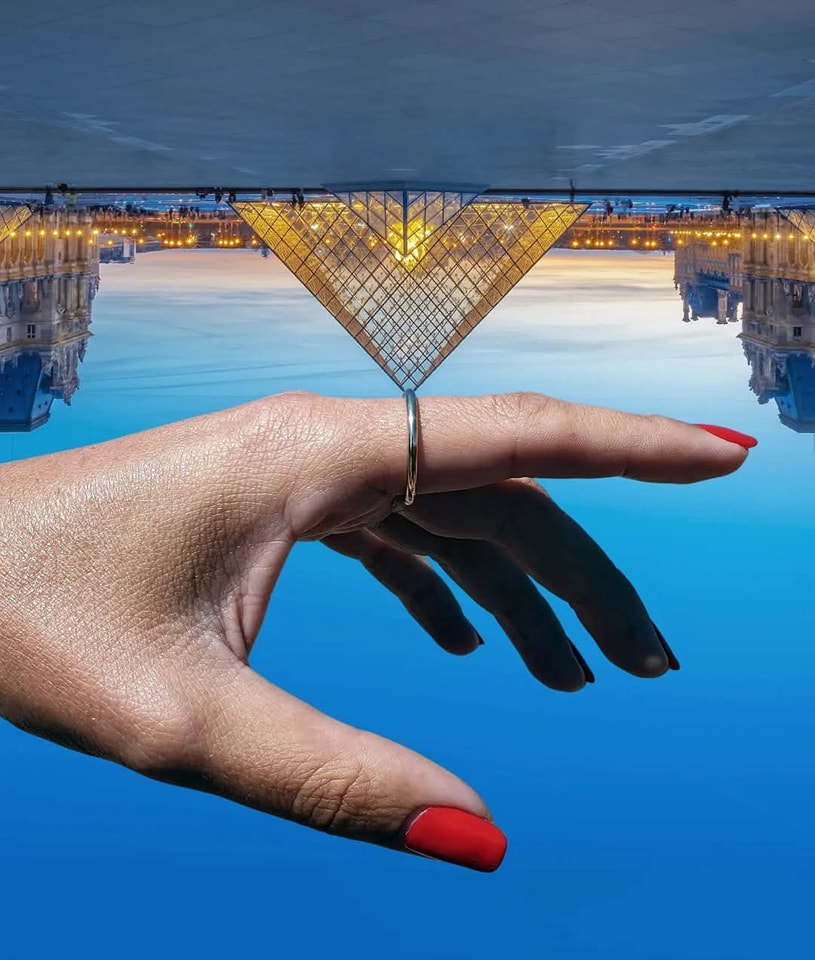 Ruka s červenými nechtami a prsteňom drží obrátenú pyramídu na modrom pozadí.