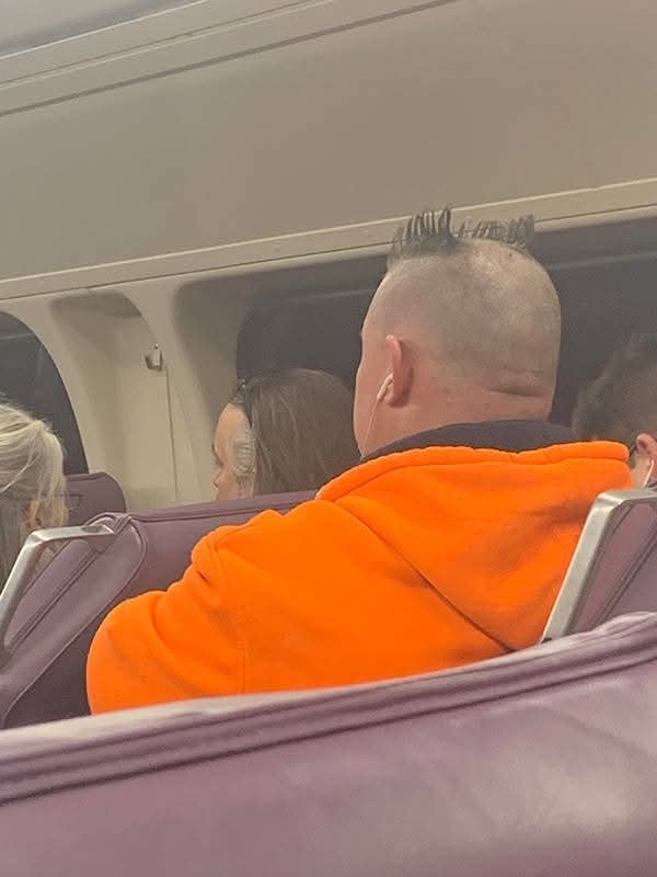 Osekaný účes a oranžová mikina cestujúceho v hromadnej doprave.