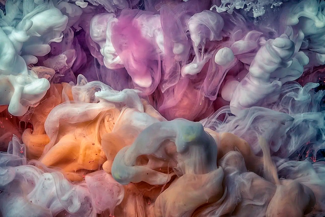 Farebný dym vznášajúci sa vo vode, vytvárajúci fascinujúce vzory v odtieňoch ružovej, fialovej a oranžovej.