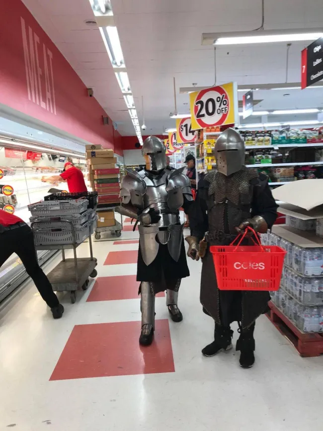 Dva rytiersky oblečení muži nakupujú v supermarkete, nesú nákupný košík a prechádzajú popri zľave 20%.