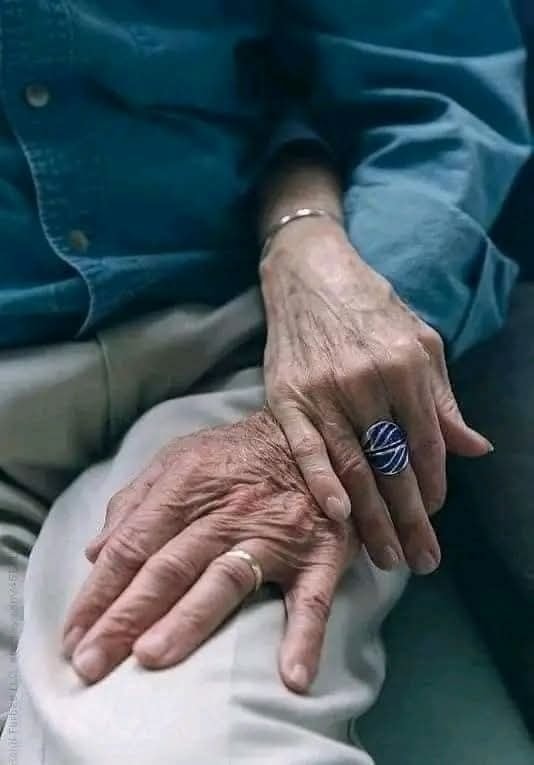 Starší pár si drží ruky, symbolizujúci lásku a vernosť v pokročilom veku.