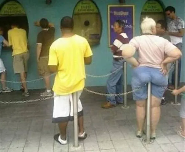 Ľudia čakajú v rade pri okienku, spočívajúc na zábranách.