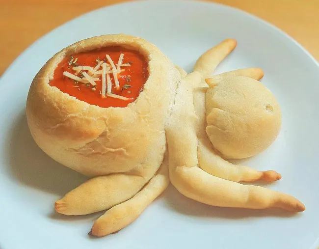 Chlebový pavúk s misou polievky a syrom na bielom tanieri, kreatívne servírovanie jedla.