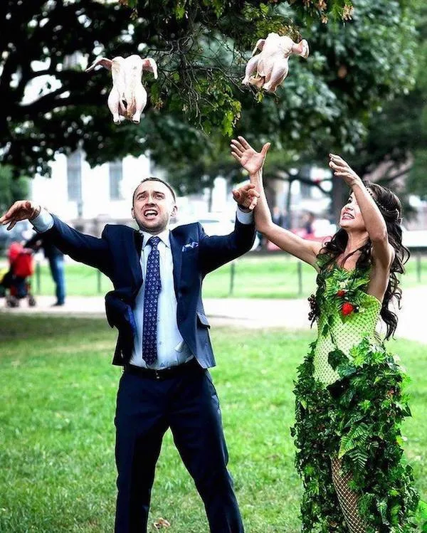 Pár v parku hádže do vzduchu surové kurčatá, oblečení vo formálnych šatách a šaty s prírodnými dekoráciami.