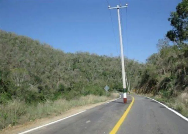 Cesta so stĺpom uprostred, obkolesená prírodou a kopcovitým terénom, modrá obloha, zelená vegetácia.