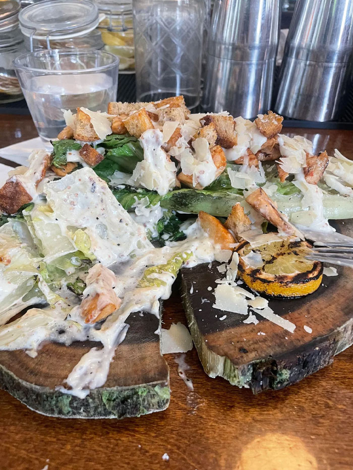 Chutný Caesar šalát so syrom, krutónmi a pečeným citrónom podávaný na drevenom podnose.