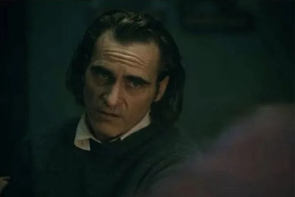 Osoba v tmavom svetri sedí v tlmenom svetle a zamyslene sa pozerá pred seba.