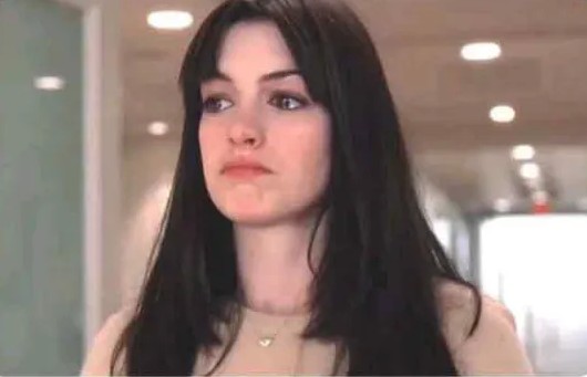 Neznáma žena s tmavými vlasmi v kancelárskom prostredí, jemne ružové tričko, pohľad smerom doprava.