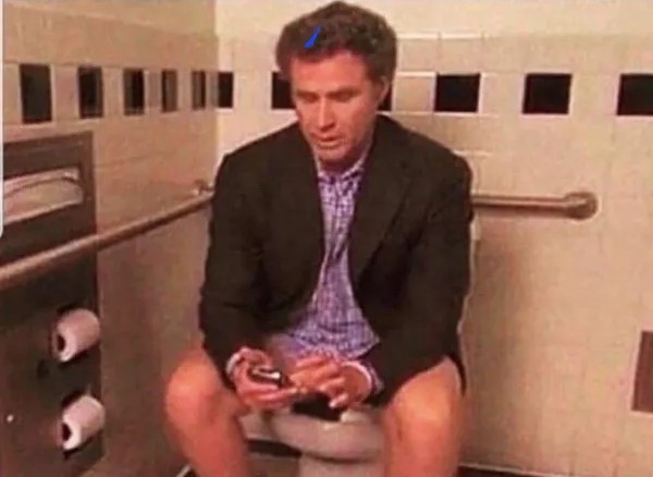 Oblečený muž na toalete, sediaci na záchode a používajúci mobilný telefón, okolo sú rolky toaletného papiera.