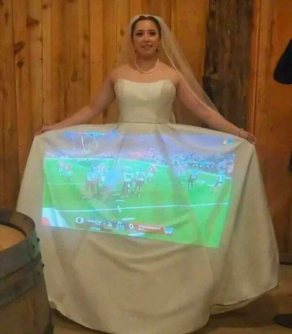 Nevesta s projektorom premietajúcim futbalový zápas na svadobné šaty, drevené pozadie.