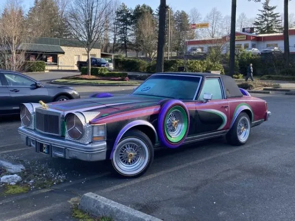 Unikátne klasické auto s pestrofarebnými detailmi zaparkované na parkovisku v mestskom prostredí.