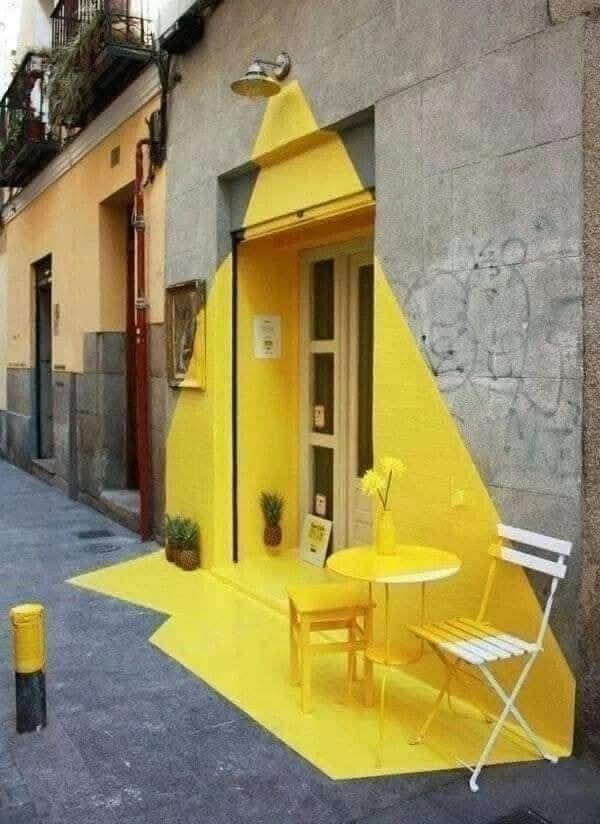 Žltý exteriér kaviarne s nábytkom a dekorom vo forme svetelného kužeľa na šedom podklade.