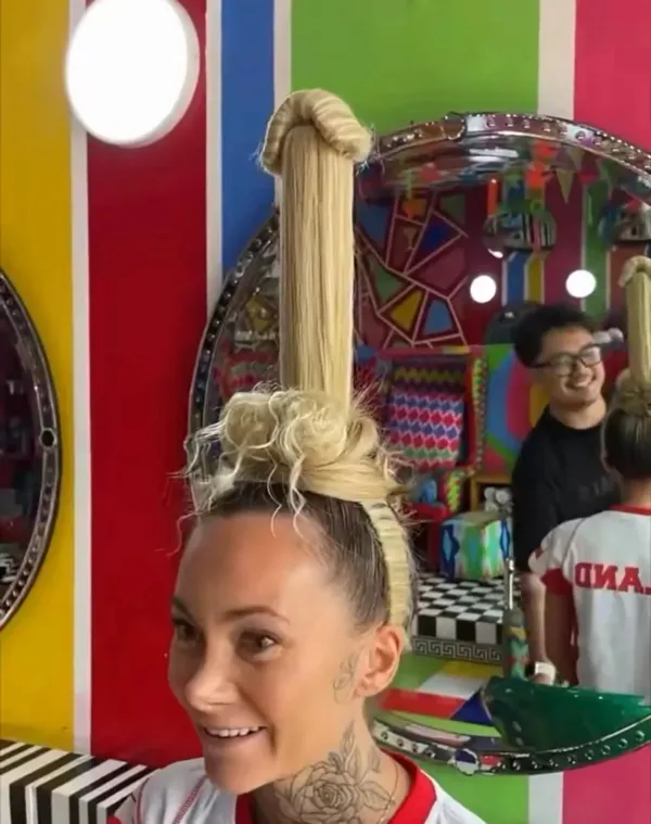 Osoba s extravagantným účesom v pestrých farbách v holičstve s geometrickými vzormi na stenách.