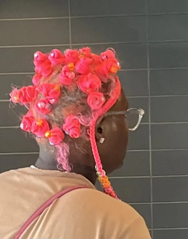 Ružové vlasy s kvetinovými uzlami, pohľad zozadu na osobu pri tmavosivom pozadí.