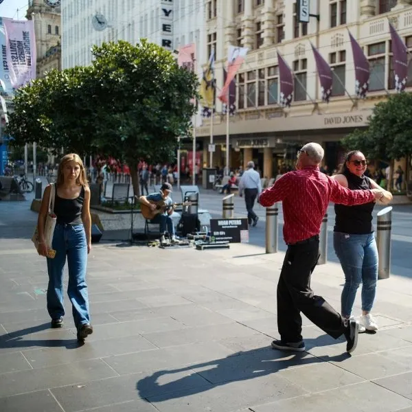 Ľudia tancujú na ulici za denného svetla vedľa pouličného hudobníka pred obchodným domom.