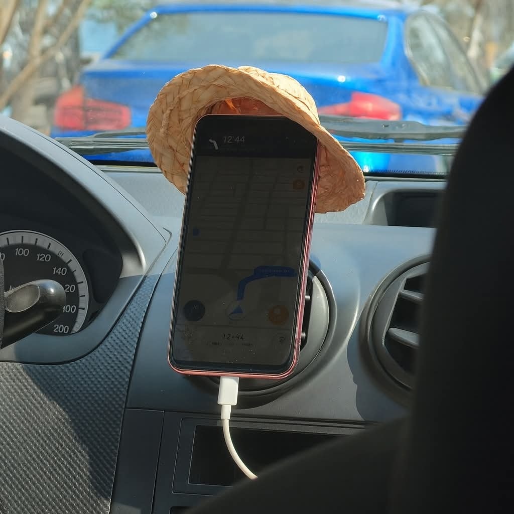 Smartfón v aute s navigáciou nabíjaný v držiaku, ozdobený klobúkom v tvare slnka.