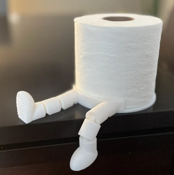 Rolka toaletného papiera s plastovými nohami na stole, slúžiaca ako vtipný držiak alebo dekorácia.
