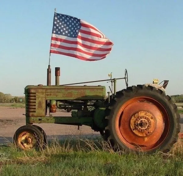 Starý traktor so zástavou USA v poli za slnečného dňa.