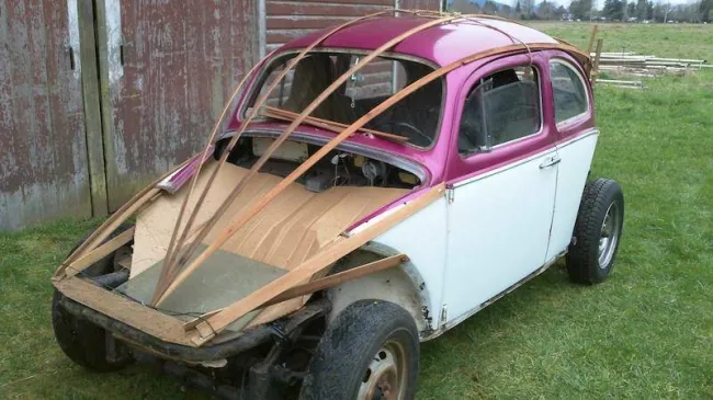 Staré auto bez kapoty s drevenou konštrukciou na opravu karosérie, stojace na trávniku.