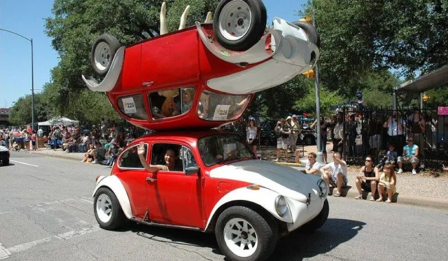 Červené auto s dvojpodlažnou karosériou na streche vystavené na ulici počas slnečného dňa a sledované ľuďmi.