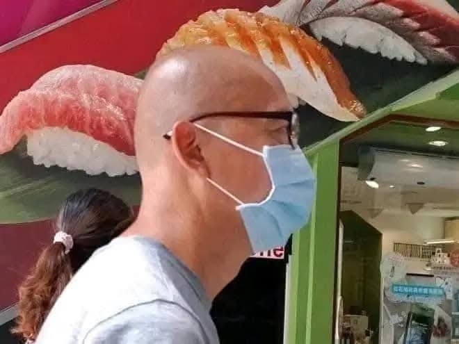 Muž v maske prechádza okolo sushi reklamy v nákupnom centre.