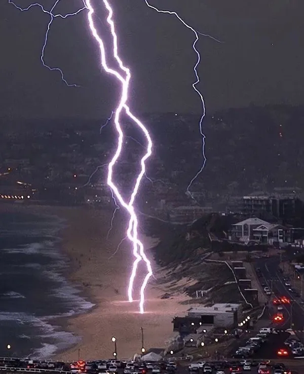 Blesk udierajúci na pláž v noci, osvetľujúci oblohu a pobrežie.