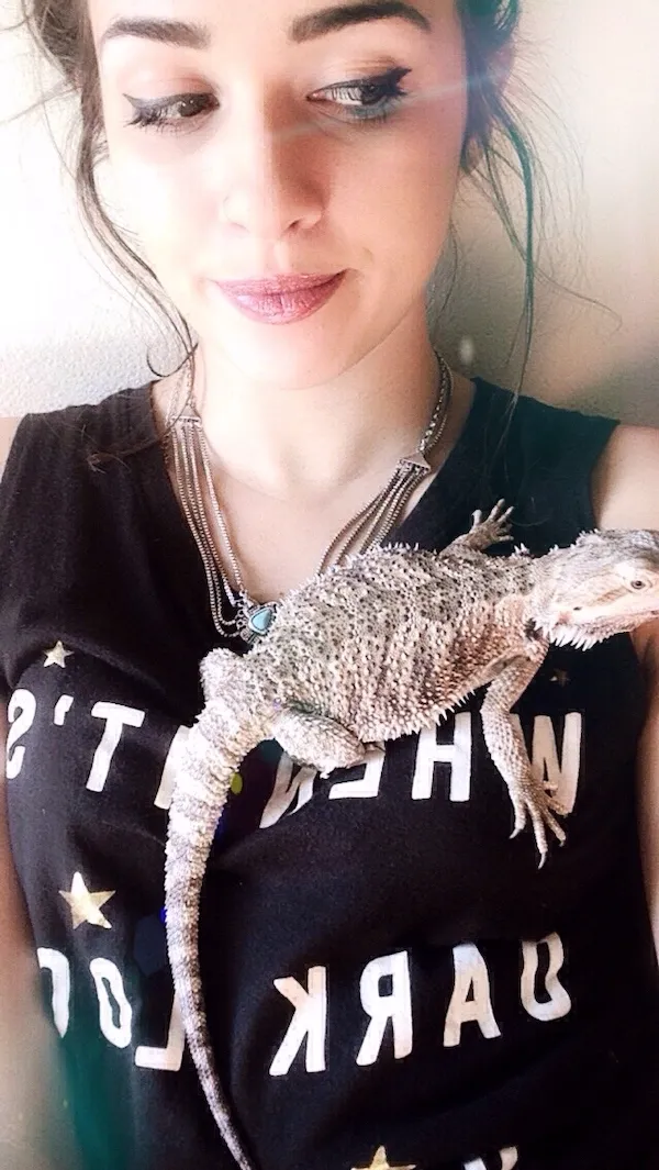 Žena s varanom na ramene, oblečená v čiernom tričku s nápisom.