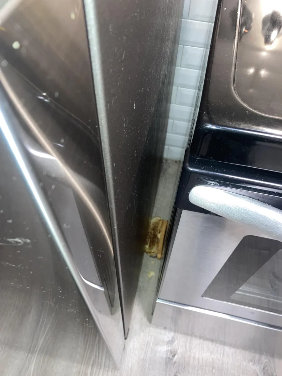 Medzera medzi chladničkou a rúrou v kuchyni, koreň usadeného nečistoty na podlahe.