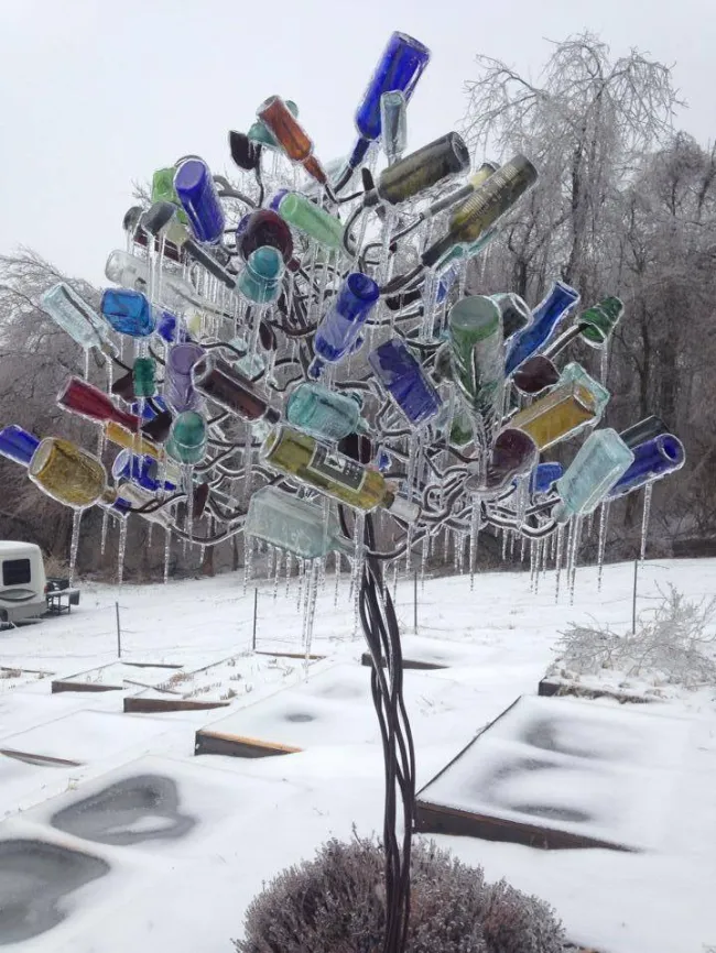 Farebný strom z fliaš v zime pokrytý ľadom v zasneženej záhrade.