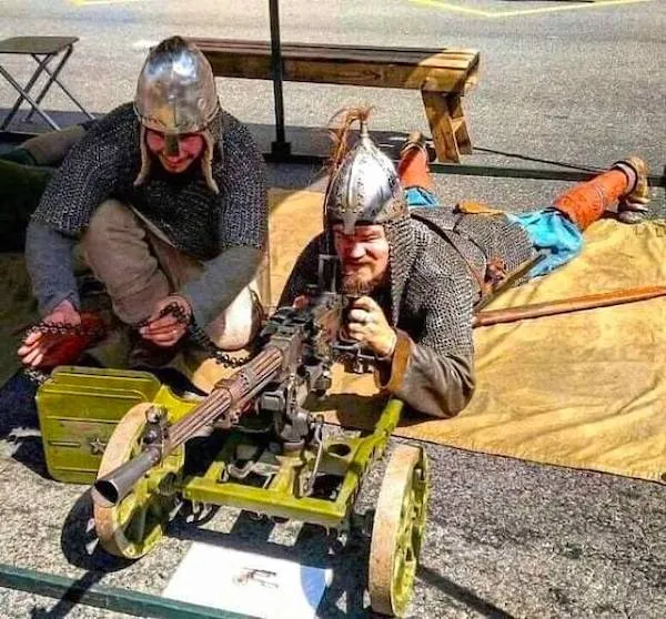 Dvaja muži v historických kostýmoch s prilbami skúšajú starý samopal na kolieskach.