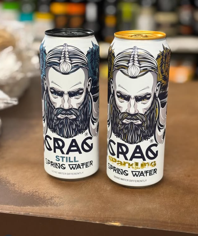 Dve plechovky minerálnej vody Crag, sýtené a nesýtené, s výrazným dizajnom na drevenom pozadí.