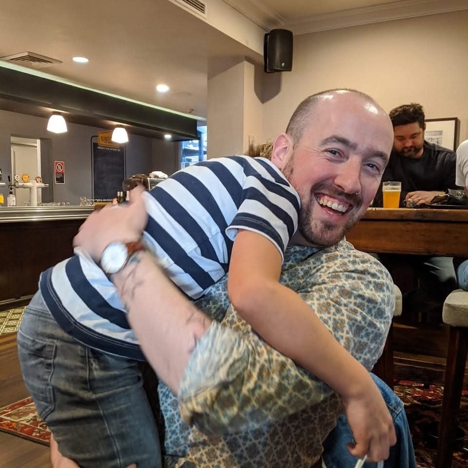 Muž s úsmevom objíma dieťa v pruhovanom tričku v útulnej reštaurácii.